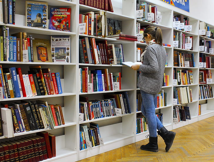 woman reading book near shelves